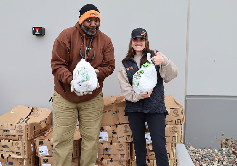 Two Curbside Waste volunteers holding frozen turkeys for a community holiday giveaway event